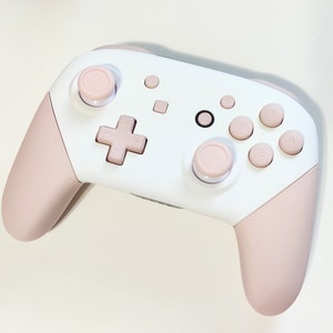 May include: A white and pink Nintendo Switch controller with pink buttons and joysticks.