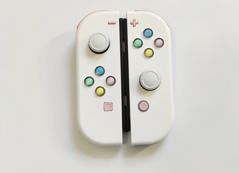 Puede incluir: Un mando Nintendo Switch Joy-Con blanco con botones de colores pastel. El mando est&aacute; en posici&oacute;n cerrada, con los lados izquierdo y derecho visibles.