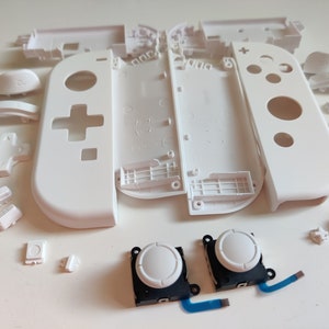 May include: White replacement parts for a Nintendo Switch console. The parts include the faceplate, buttons, and joysticks.
