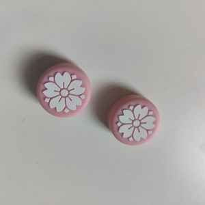 May include: Two pink, circular objects with a white floral design. The objects are likely decorative or functional, possibly buttons or knobs. The image is taken from a top-down perspective.