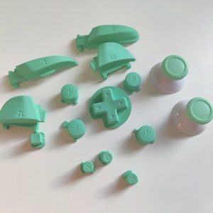 May include: A set of green replacement buttons for a video game controller. The buttons include the standard face buttons, shoulder buttons, and analog stick caps.