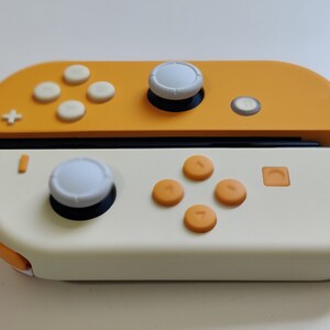 Puede incluir: Un mando de Nintendo Switch amarillo y blanco con un bot&oacute;n blanco en la parte superior y botones naranjas en la parte inferior.