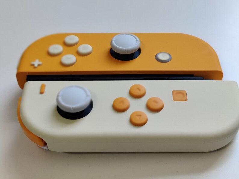 Puede incluir: Un mando de Nintendo Switch amarillo y blanco con un bot&oacute;n blanco en la parte superior y botones naranjas en la parte inferior.