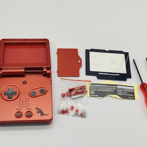 May include: A red Game Boy Advance SP console with a dinosaur graphic on the front. The console is disassembled and laid out on a white surface with replacement parts, including a screen, faceplate, screws, and screwdrivers.
