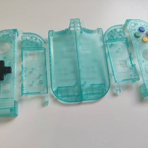 Könnte beinhalten: Ein Satz tealblauer Kunststoff-Ersatzschalen für eine Spielekonsole. Die Schalen sind zerlegt und zeigen die verschiedenen Teile, darunter die Fronttasten, die Rückwand und die Seitenwände.