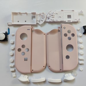 May include: A set of replacement parts for a Nintendo Switch console. The set includes two pink joy-con shells, a white faceplate, and various buttons and other components.