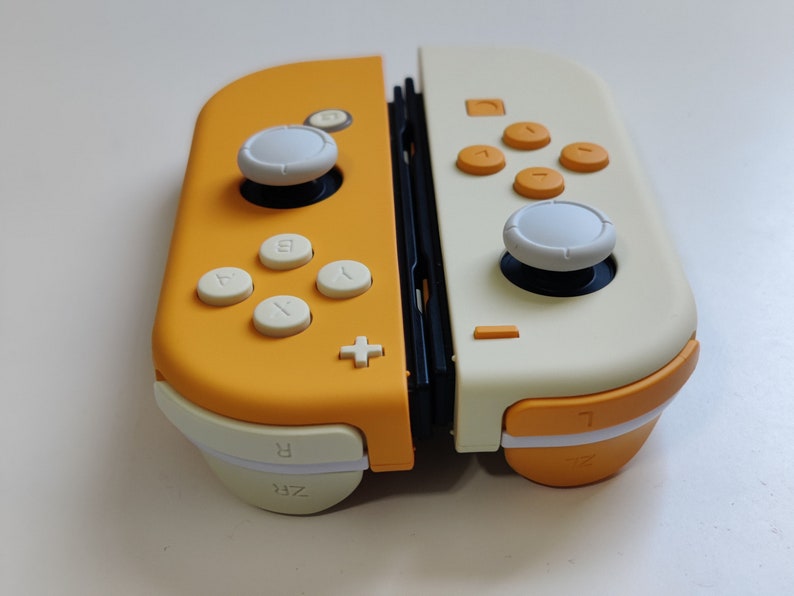 Puede incluir: Un mando de Nintendo Switch amarillo y blanco con botones y joysticks blancos. El mando tiene una secci&oacute;n central negra y las palabras "ZR" y "R" est&aacute;n impresas en la parte inferior.
