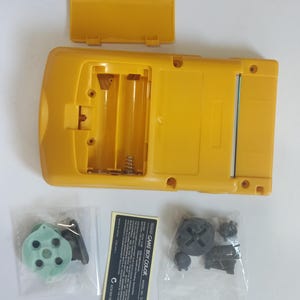 K&ouml;nnte beinhalten: Gelbe Game Boy Color Handheld-Spielkonsole mit ge&ouml;ffnetem Batteriefach. Enth&auml;lt Ersatzteile in kleinen Plastikt&uuml;ten und einen Produktinformationsaufkleber. Die Konsole ist gelb.