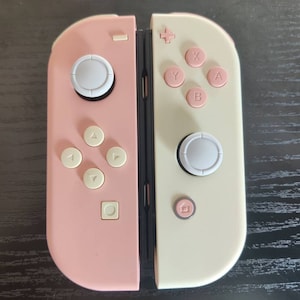 May include: A pink and white Nintendo Switch Joy-Con controller with white buttons and a pink and white design.