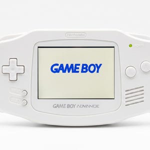 May include: A white handheld video game console with a central screen displaying the blue text GAME BOY. The device features a directional pad on the left, two circular buttons on the right, and the text GAME BOY ADVANCE printed below the screen.