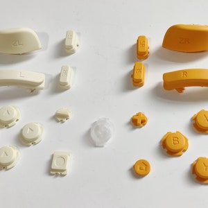 Könnte beinhalten: Ein Satz Ersatztasten für einen Videospiel-Controller. Die Tasten sind in zwei Farben: weiß und orange. Die weißen Tasten haben die Buchstaben "L", "R", "ZL", "ZR", "SL", "SR" und Pfeile. Die orangen Tasten haben die Buchstaben "A", "B", "Y", "X" und ein Pluszeichen.