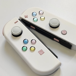 Puede incluir: Un mando Nintendo Switch Joy-Con blanco con botones de colores pastel. El mando est&aacute; en dos partes, con los lados izquierdo y derecho separados.