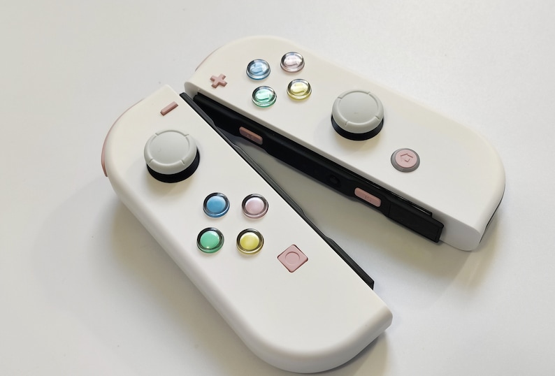 Puede incluir: Un mando Nintendo Switch Joy-Con blanco con botones de colores pastel. El mando est&aacute; en dos partes, con los lados izquierdo y derecho separados.
