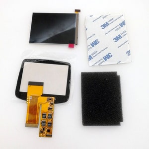 May include: A replacement screen kit for a handheld gaming device. The kit includes a black LCD screen, a clear plastic screen protector, a gold ribbon cable, a circuit board, a black foam pad, and two sheets of adhesive tape labelled "3M 9448A Double Coated Tissue Tape".