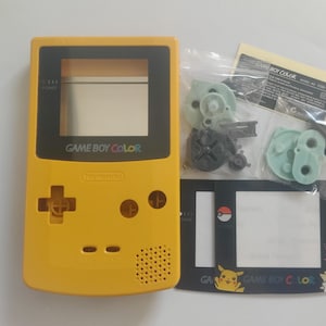 Könnte beinhalten: Gelbe Game Boy Color Konsole mit schwarzen Akzenten, Nintendo-Logo und "GAME BOY COLOR" Text. Enthält Ersatzteile und eine Displayschutzfolie mit Pokémon-Grafiken. Ein Retro-Gaming-Artikel.