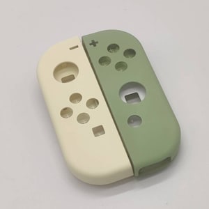 Może przedstawiać: Dwukolorowa, kremowa i zielona, zamienna obudowa do kontrolera Nintendo Switch. Obudowa zawiera wszystkie przyciski i elementy sterujące kontrolera.