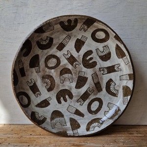 May include: A white ceramic bowl with a brown geometric pattern. The bowl is round and has a slightly raised rim.