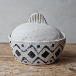 Peut inclure: Plat en céramique blanche avec couvercle, décoré d'un motif géométrique bleu et noir. Le couvercle a un bouton texturé.