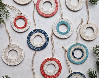 May include: Twelve ceramic Christmas ornaments with a white background and various colored designs. The ornaments are round and have a hole at the top for hanging. The designs include red, blue, and white geometric patterns.