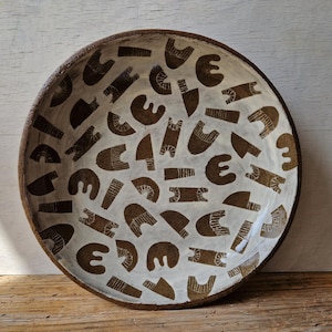 May include: A white ceramic bowl with a brown geometric pattern. The bowl is round and has a slightly raised rim.