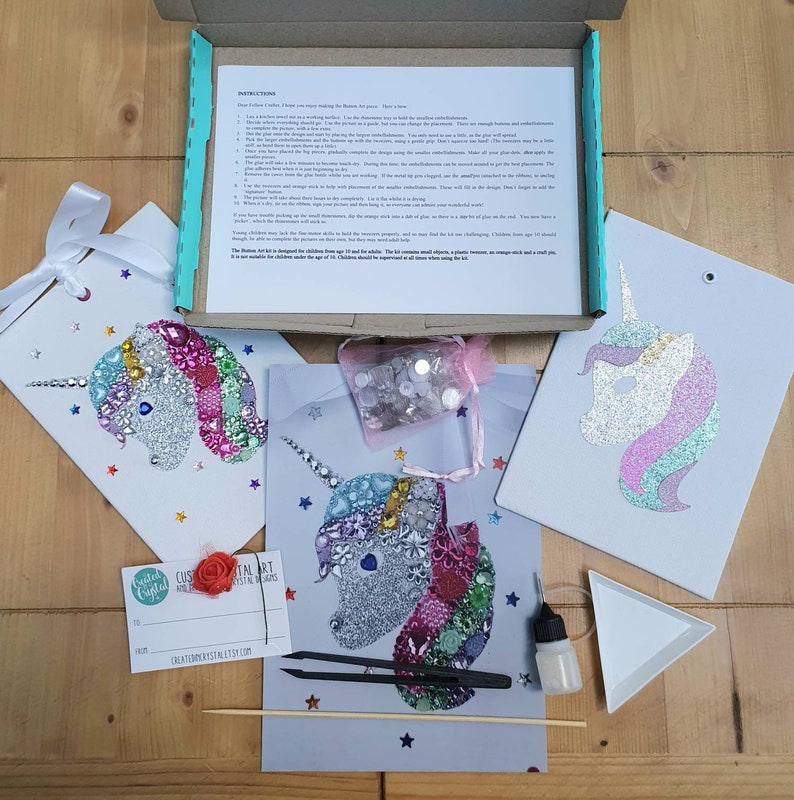 May include: A craft kit featuring three unicorn-themed art projects, a box of instructions, a small pink mesh bag of assorted embellishments, black tweezers, a small glue bottle, a white triangular tray, a wooden stick, and a gift tag.