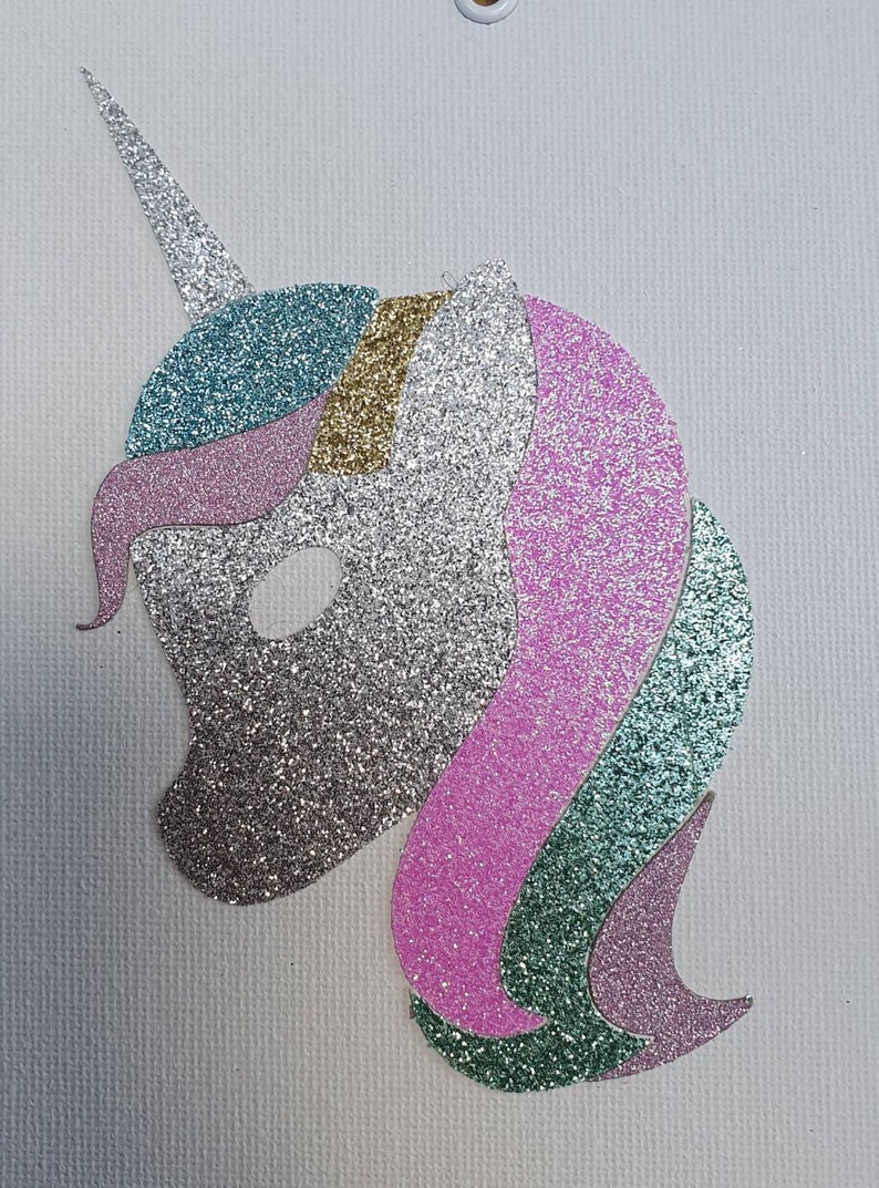 May include: A glittery unicorn head cutout featuring a silver face and horn, a teal and gold forehead section, and a flowing mane composed of layered pink, teal, and silver glitter segments. The design is flat and oriented in profile.