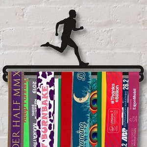 Könnte beinhalten: Schwarzer Metall-Medaillenhalter mit einer Läufer-Silhouette. Der Halter enthält eine Vielzahl von bunten Laufmedaillen mit Texten wie "2019 Marathon", "Burnbake", "Running", "6.2 ABP", "London Marathon", "#Thanks a Billion", "Southampton Marathon", "26.2", "New Forest Marathon" und "ExxonMobil".
