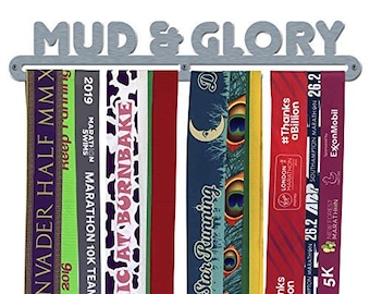 May include: A silver metal medal rack with the words "MUD & GLORY" on it. There are five medals hanging on the rack. The medals are colorful and have different designs and text. The text on the medals includes "#Thanks a Billion", "White Star Running", "26.2 ABP", "Rolic At Burnbake", and "Invader Half MMX".