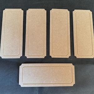 May include: Six unfinished rectangular wooden plaques with decorative edges are displayed. The plaques are arranged on a dark surface, with five standing vertically and one lying horizontally. The wood has a light brown colour.