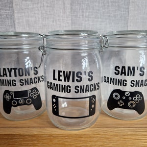 May include: Three clear glass jars with black lids and labels. The labels say "Layton's Gaming Snacks", "Lewis's Gaming Snacks", and "Sam's Gaming Snacks". Each jar has a black graphic of a video game controller.