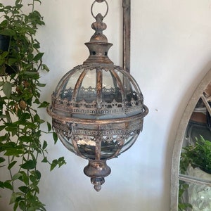 May include: An antique-style wall lantern with a globe-shaped glass enclosure and decorative metalwork. The metal has a distressed finish. The lantern is mounted on a curved arm. The overall design suggests a vintage aesthetic, suitable for indoor or outdoor use.