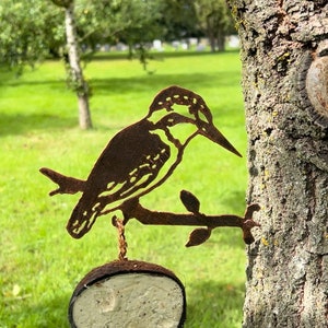 May include: A metal bird feeder shaped like a kingfisher perched on a branch. The feeder is attached to a tree trunk and has a round, white suet cake hanging from it.