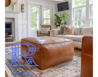 May include: A brown leather ottoman with a square shape sits on a patterned rug in a living room. The ottoman is in front of a white couch with throw pillows.