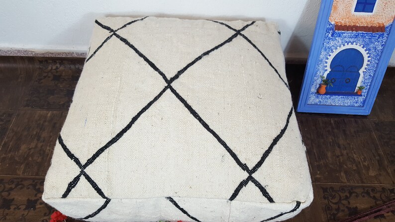 Puede incluir: Un coj&iacute;n de suelo blanco con patrones de diamantes negros. El coj&iacute;n est&aacute; hecho de una tela suave y tejida.
