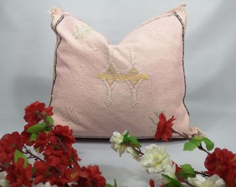 May include: A pink throw pillow with a geometric pattern and a fringe border. The pillow is made of a soft, woven fabric and has a subtle sheen.