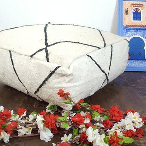 Puede incluir: Un coj&iacute;n de suelo blanco con patrones geom&eacute;tricos negros. El coj&iacute;n est&aacute; hecho de un material suave y esponjoso y tiene una forma cuadrada.