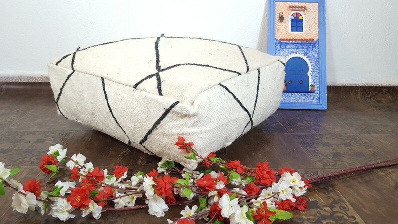 Puede incluir: Un coj&iacute;n de suelo blanco con patrones geom&eacute;tricos negros. El coj&iacute;n est&aacute; hecho de un material suave y esponjoso y tiene una forma cuadrada.