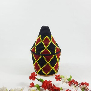 K&ouml;nnte beinhalten: Ein geflochtener Korb in Schwarz und Rot mit einem gelben Rautenmuster. Der Korb ist kegelf&ouml;rmig und hat einen runden Boden.