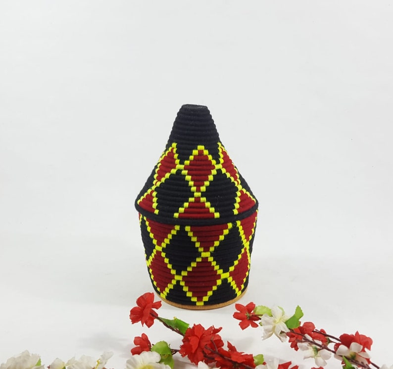 K&ouml;nnte beinhalten: Ein geflochtener Korb in Schwarz und Rot mit einem gelben Rautenmuster. Der Korb ist kegelf&ouml;rmig und hat einen runden Boden.