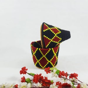 K&ouml;nnte beinhalten: Ein gewebter Aufbewahrungsbeh&auml;lter in Schwarz, Rot und Gelb mit Deckel. Der Beh&auml;lter hat ein Diamantenmuster.