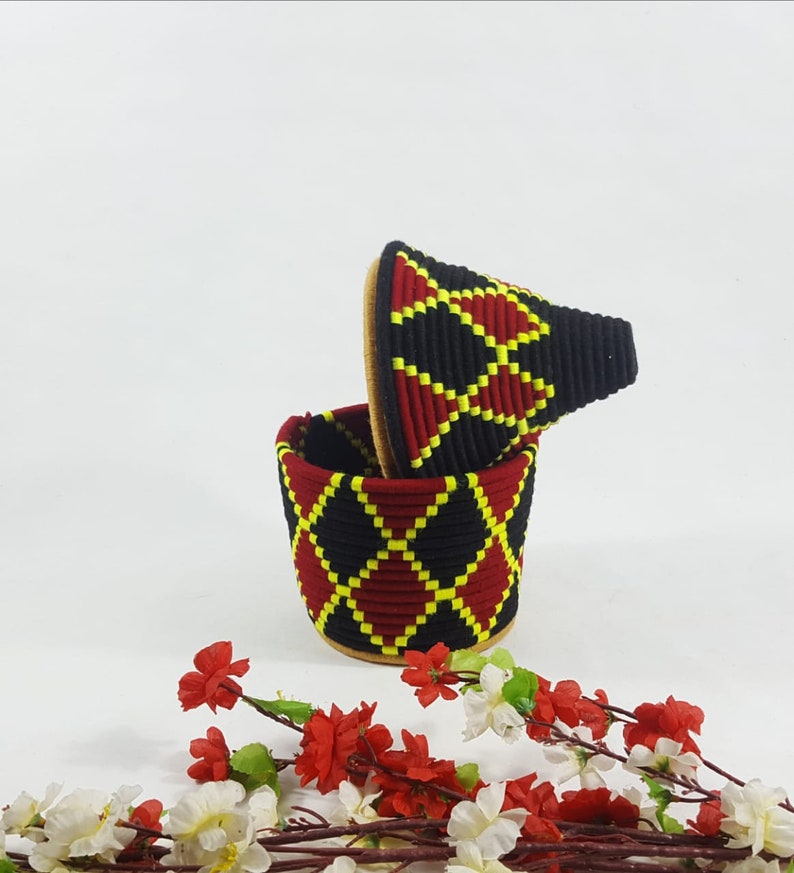 K&ouml;nnte beinhalten: Ein gewebter Aufbewahrungsbeh&auml;lter in Schwarz, Rot und Gelb mit Deckel. Der Beh&auml;lter hat ein Diamantenmuster.