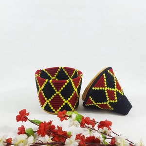 K&ouml;nnte beinhalten: Zwei geflochtene K&ouml;rbe mit einem geometrischen Muster in Rot, Schwarz und Gelb. Die K&ouml;rbe sind aus einem weichen, biegsamen Material gefertigt und haben ein einzigartiges, handgefertigtes Aussehen.