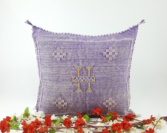 May include: A purple and white patterned throw pillow with tassels. The pillow has a geometric design with a cross shape in the center.