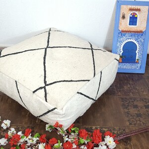 Puede incluir: Un coj&iacute;n de suelo blanco con l&iacute;neas geom&eacute;tricas negras. El coj&iacute;n est&aacute; hecho de un material suave y esponjoso y tiene una forma cuadrada.