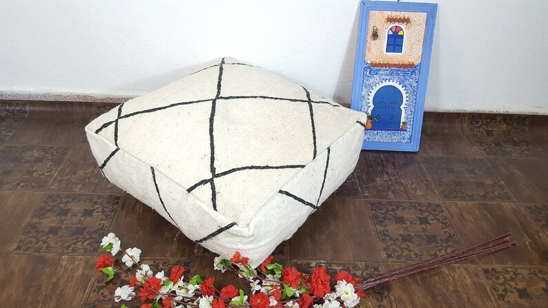 Puede incluir: Un coj&iacute;n de suelo blanco con l&iacute;neas geom&eacute;tricas negras. El coj&iacute;n est&aacute; hecho de un material suave y esponjoso y tiene una forma cuadrada.