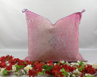 May include: Pink throw pillow with a white geometric pattern and tassels. The pillow is made of a soft, woven fabric.