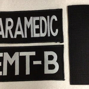 May include: Two black fabric patches with white text. The top patch reads "PARAMEDIC" and the bottom patch reads "EMT-B".
