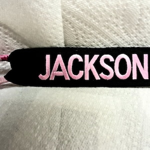 May include: A black fabric keychain with a pink metal carabiner clip. The keychain has the name "JACKSON" embroidered in pink letters.