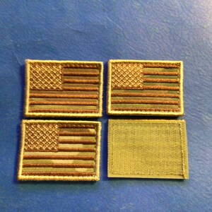 May include: Four small American flag patches with a camouflage pattern and a beige background. The patches are surrounded by a beige border. Below the patches is a beige patch with a rough texture.