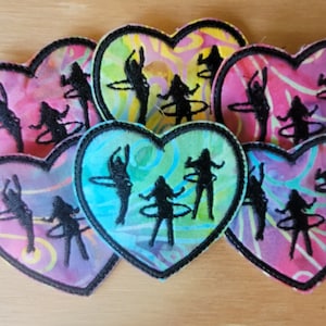 Op de afbeelding: Zes hartvormige stoffen patches met kleurrijke swirl-patronen en zwarte geborduurde silhouetten van mensen die hulahoepen.